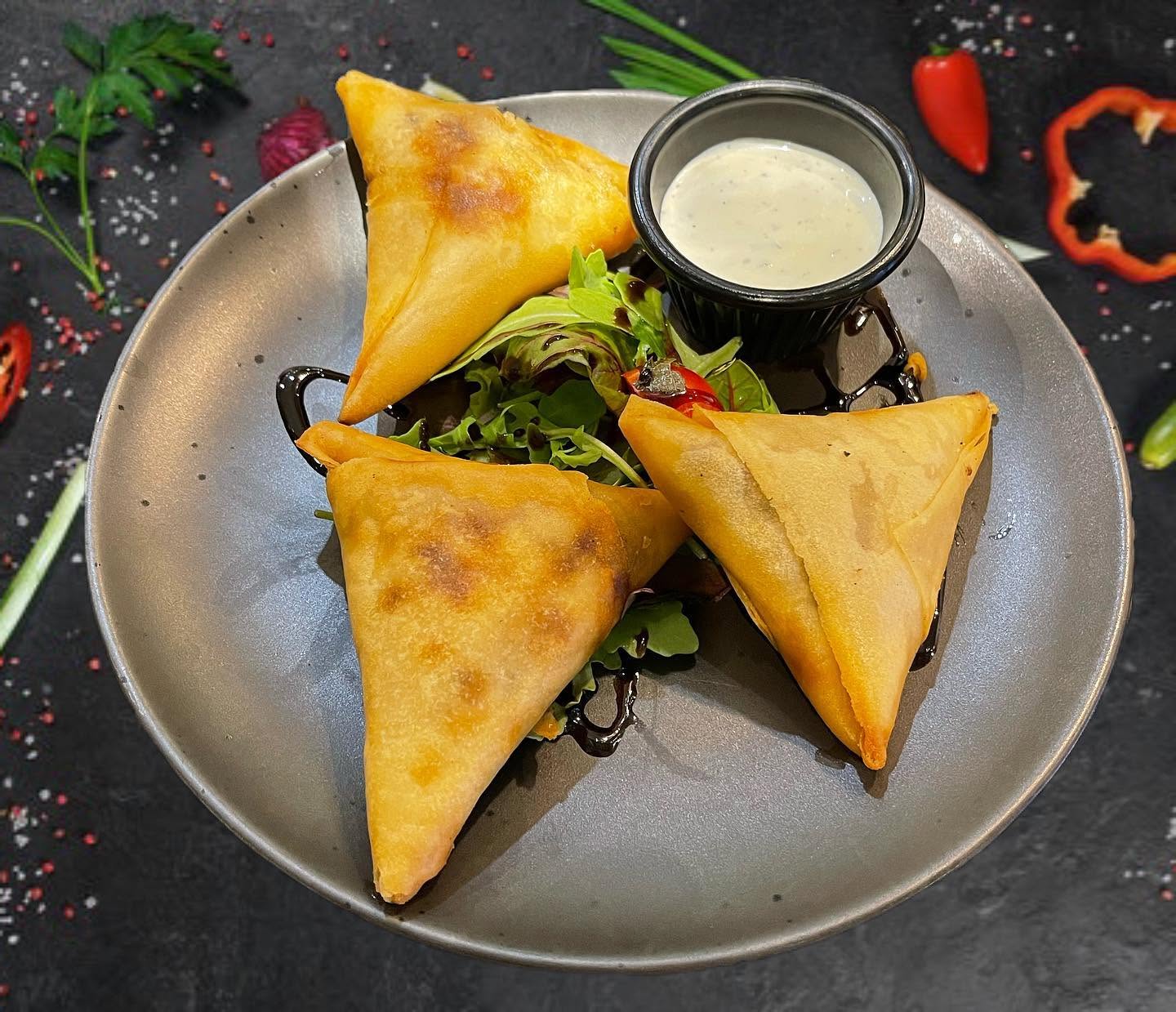  Ela restaurant's three golden crispy meat samosas served with fresh salad and a creamy dipping sauce in Stowmarket.